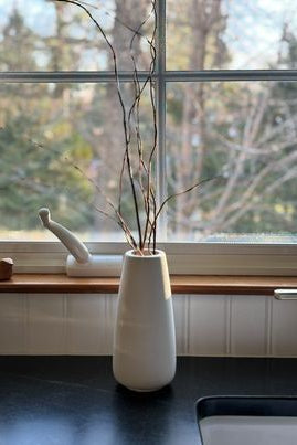 White vase on a windowsill with a view of trees outside